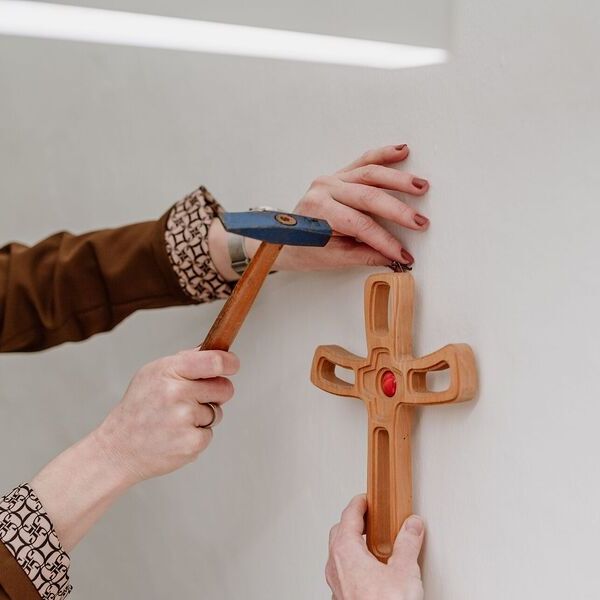 Frauen gestalten Kirche / © Diözese Linz / Frauenkommission / Laurenz Kaiser Ein hölzernes Kreuz wird an der Wand befestigt.